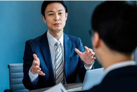 専任担当が物件を評価・売却戦略をご提案のイメージ写真。スーツ姿の男性がジェスチャーを交えて説明をしている。